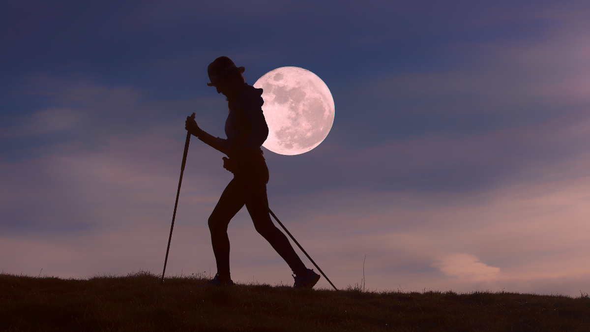 A person hikes with a full moon in the background