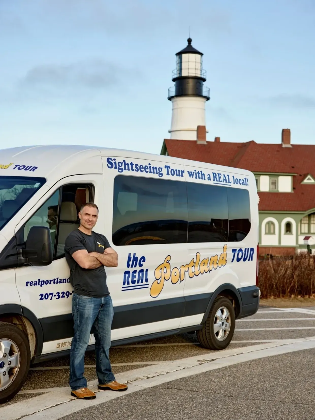 Derek from the Real Portland Tour stands next to his tour guide van in front of Portland Head Light in portland, Maine.